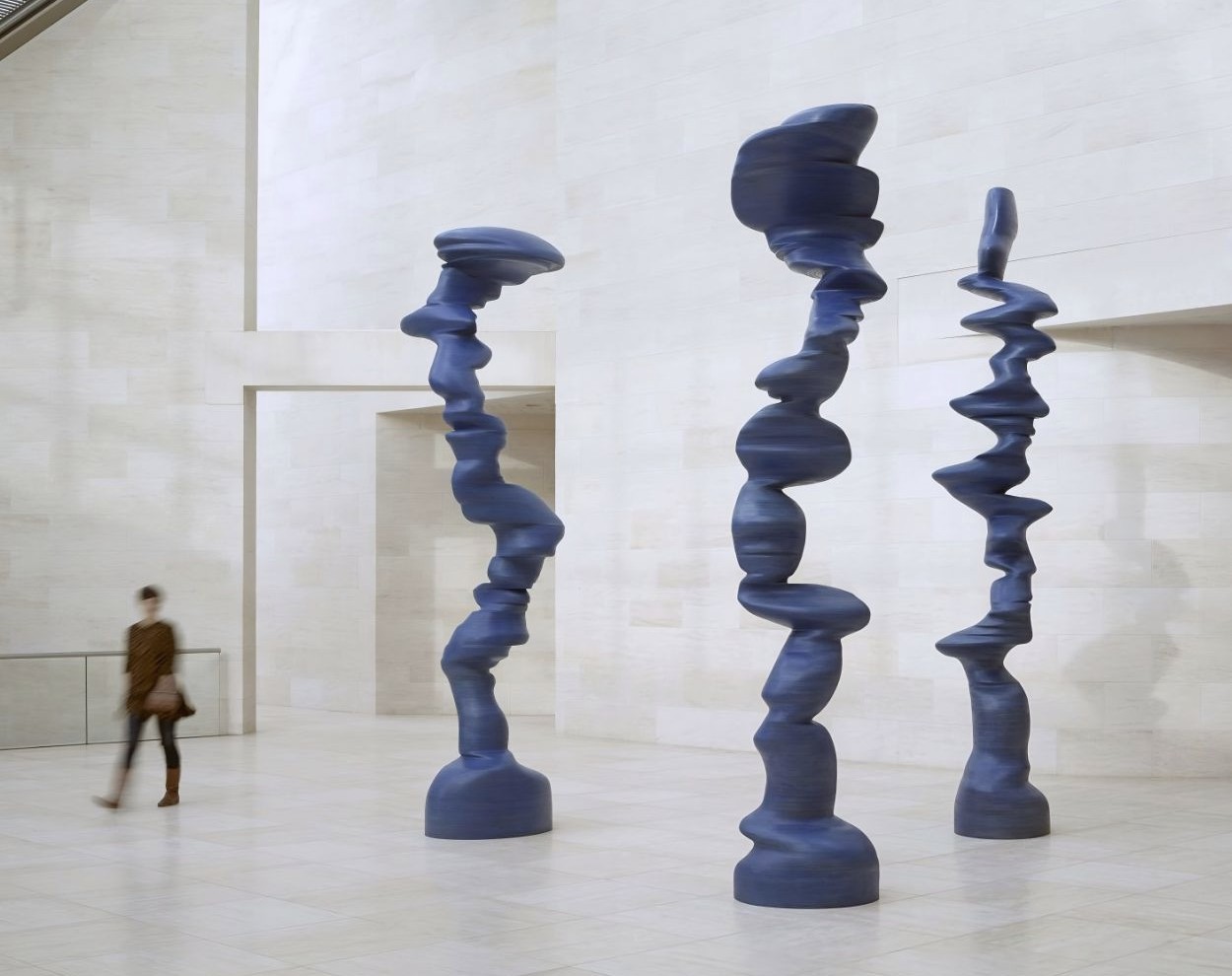 Three of Tony Cragg's blue stacked sculptures standing in a pale stone hall