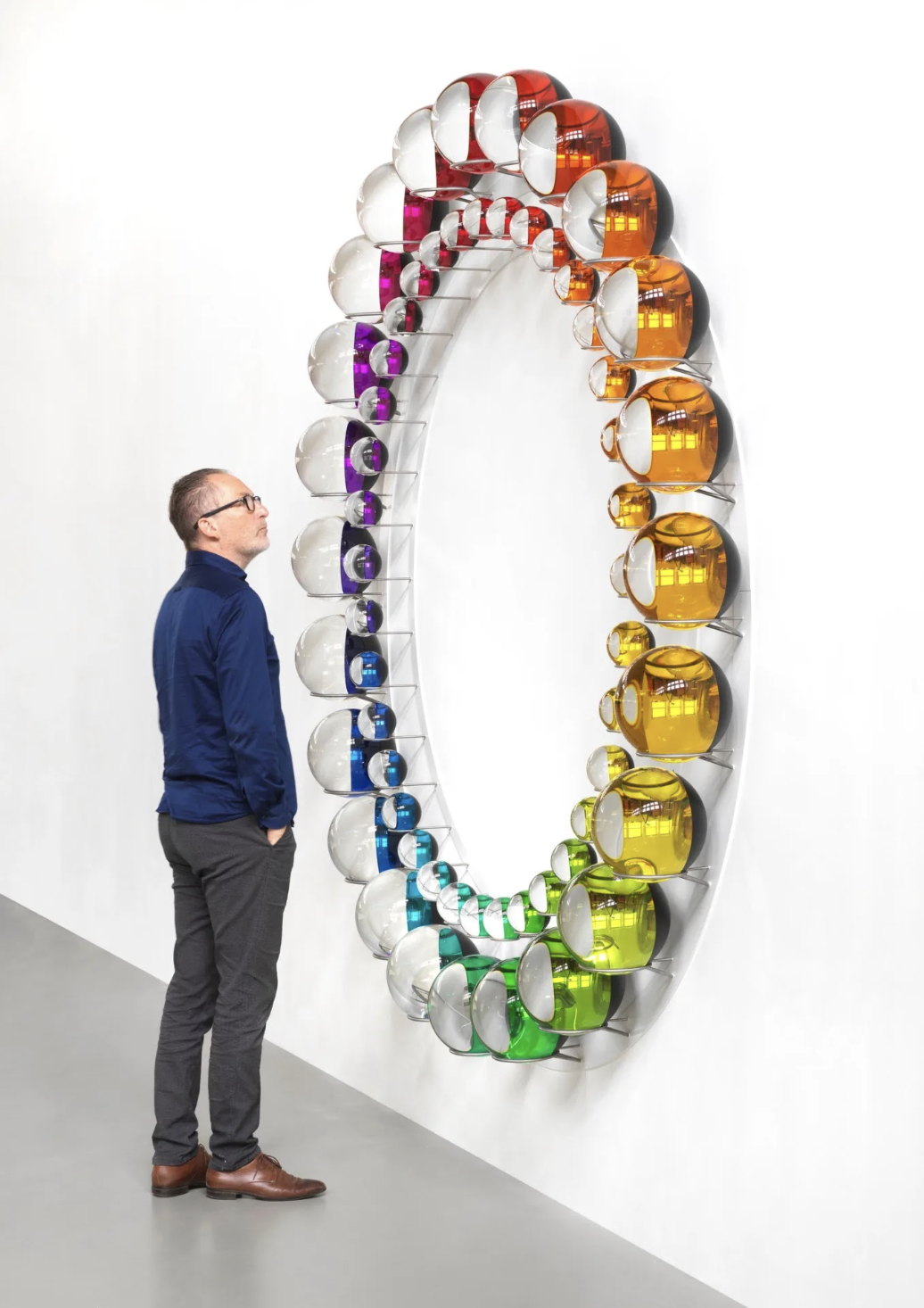 A man looking up at a ring of coloured glass spheres